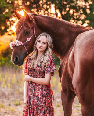 Kobieta w czerwonej sukience pozuje z koniem udekorowanym kwiatami o zachodzie słońca