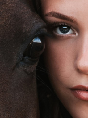 Zbliżenie oka konia i twarzy kobiety patrzącej w obiektyw