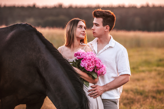 Para młoda z koniem pozuje na złocistej łące o zachodzie słońca