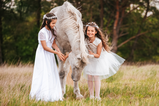 Dziewczynka w białej sukience głaszcze białego konia na tle zielonego krajobrazu