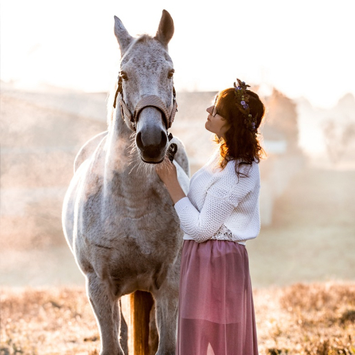 Dziewczyna z białek bluzce z wiankiem na włosach trzyma jasnego konia